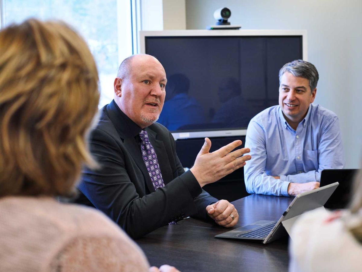 Two man and woman in a meeting room with a laptop and TV