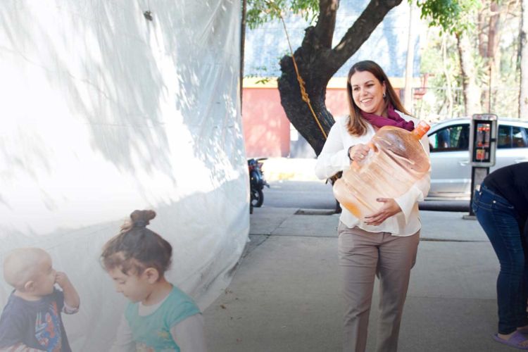 woman carrying a large jerry can full of water while walking down a street