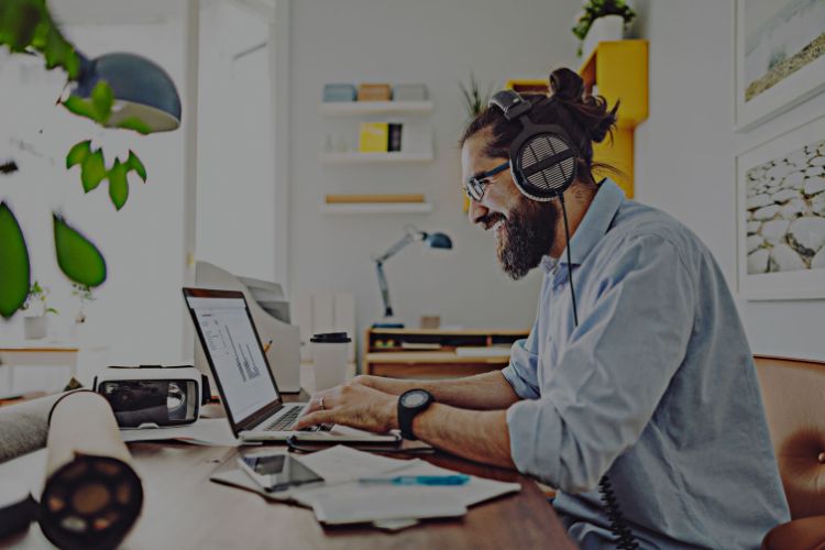Man in a shirt sitting at a desk working on a laptop with headphones on