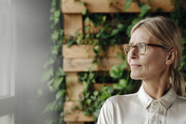 Woman in front of wooden, leafy background looking into the distance