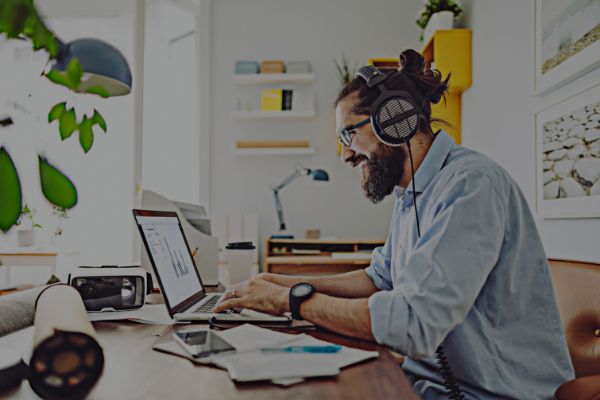 Man in a shirt sitting at a desk working on a laptop with headphones on